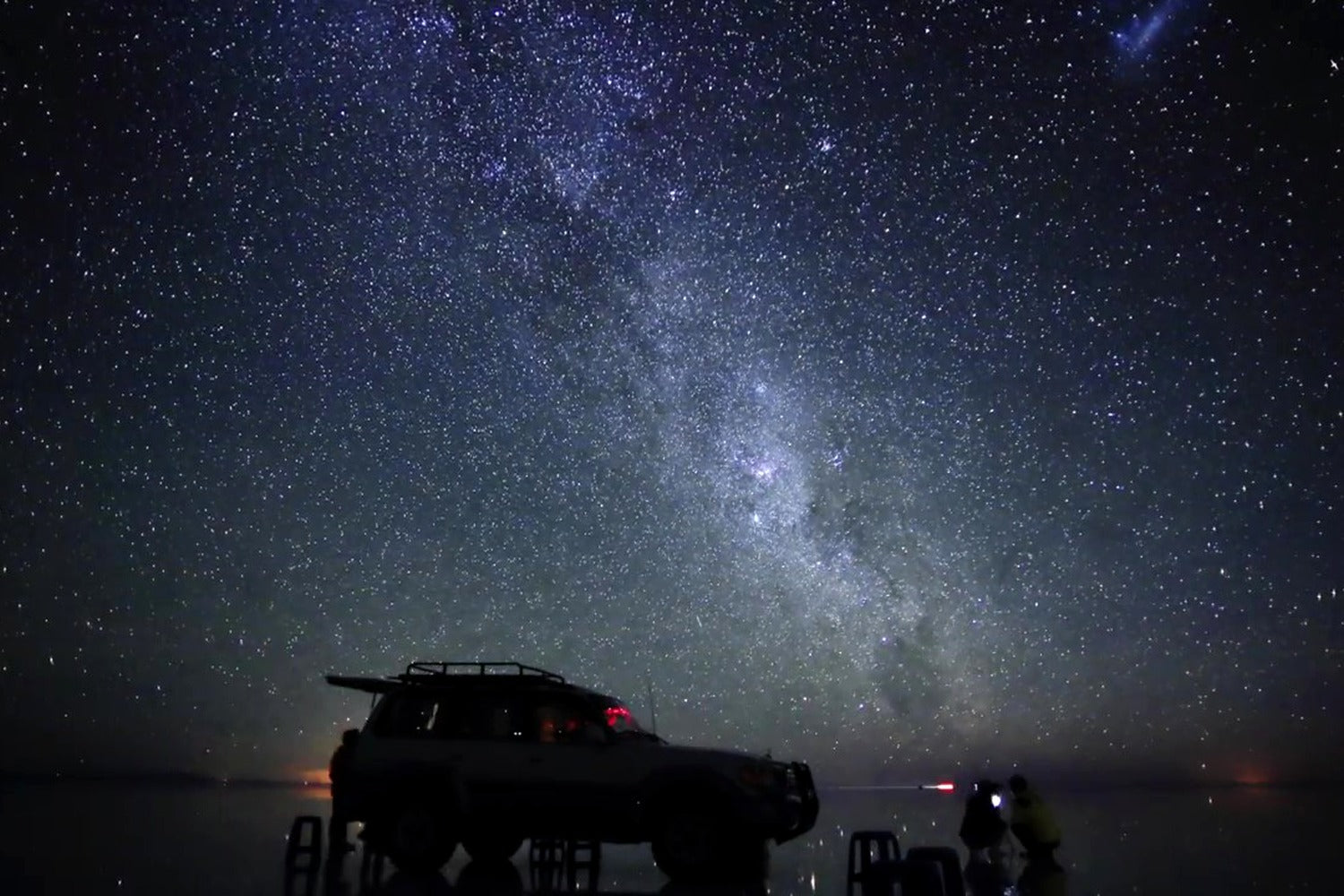 Car and person under a starry night sky with the Milky Way at Uyuni salt flat, Bolivia.
