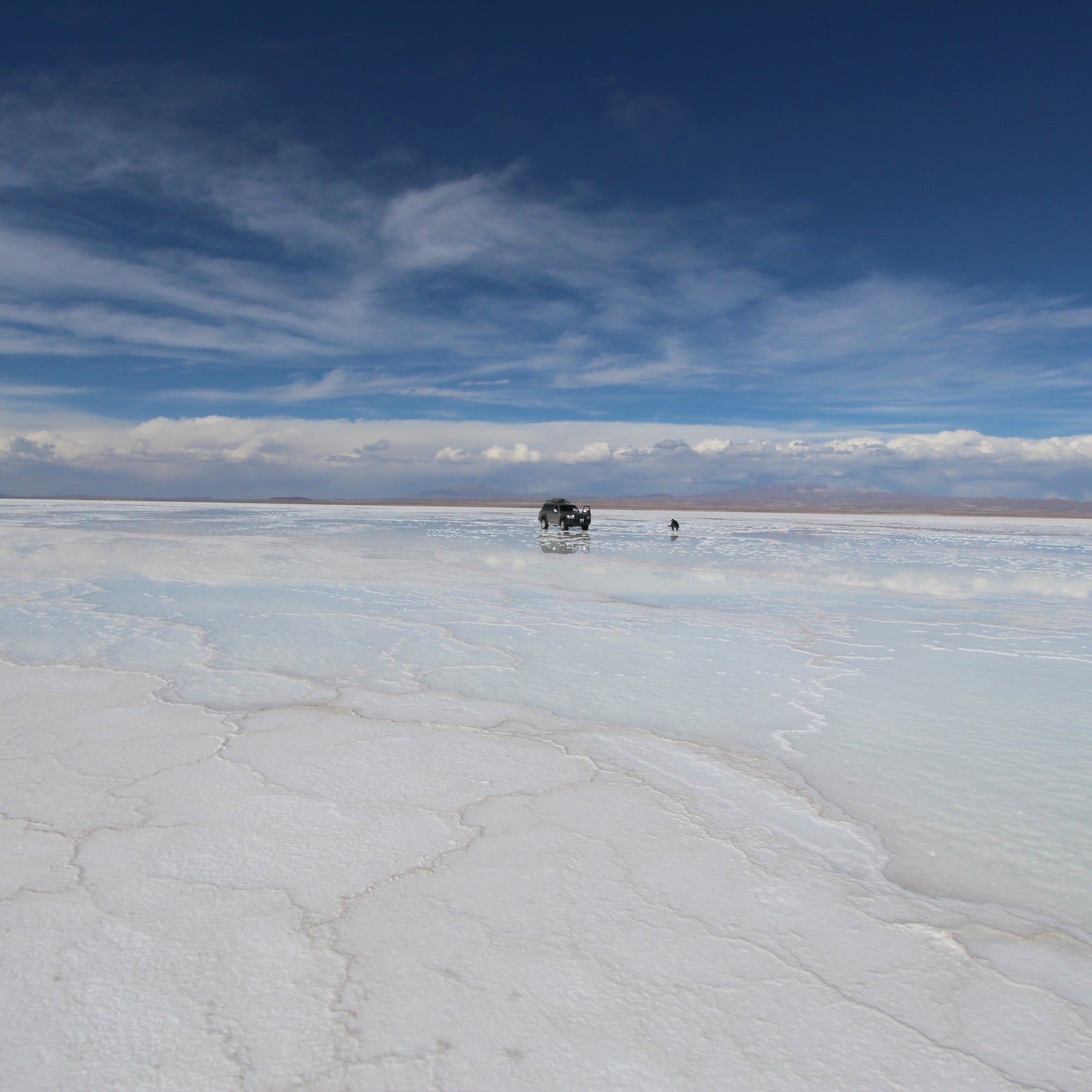 4x4 stopped at Uyuni salt flat with  with a clear blue sky and a few scattered clouds.