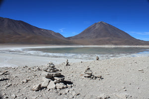 Desert landscape at South Lipez with mountains and a lake, featuring stone cairns.