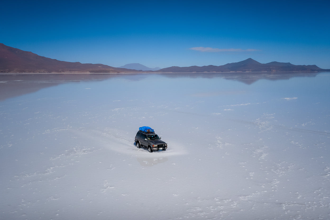 Aerial view of a 4x4 crossing a shallow reflective layer on the Uyuni Salt Flat, Bolivia