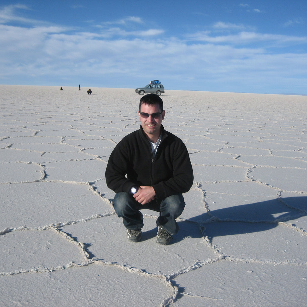 Alistair Kelly crouching on the Uyuni Salt Flat with a 4x4 and travelers in the distance.
