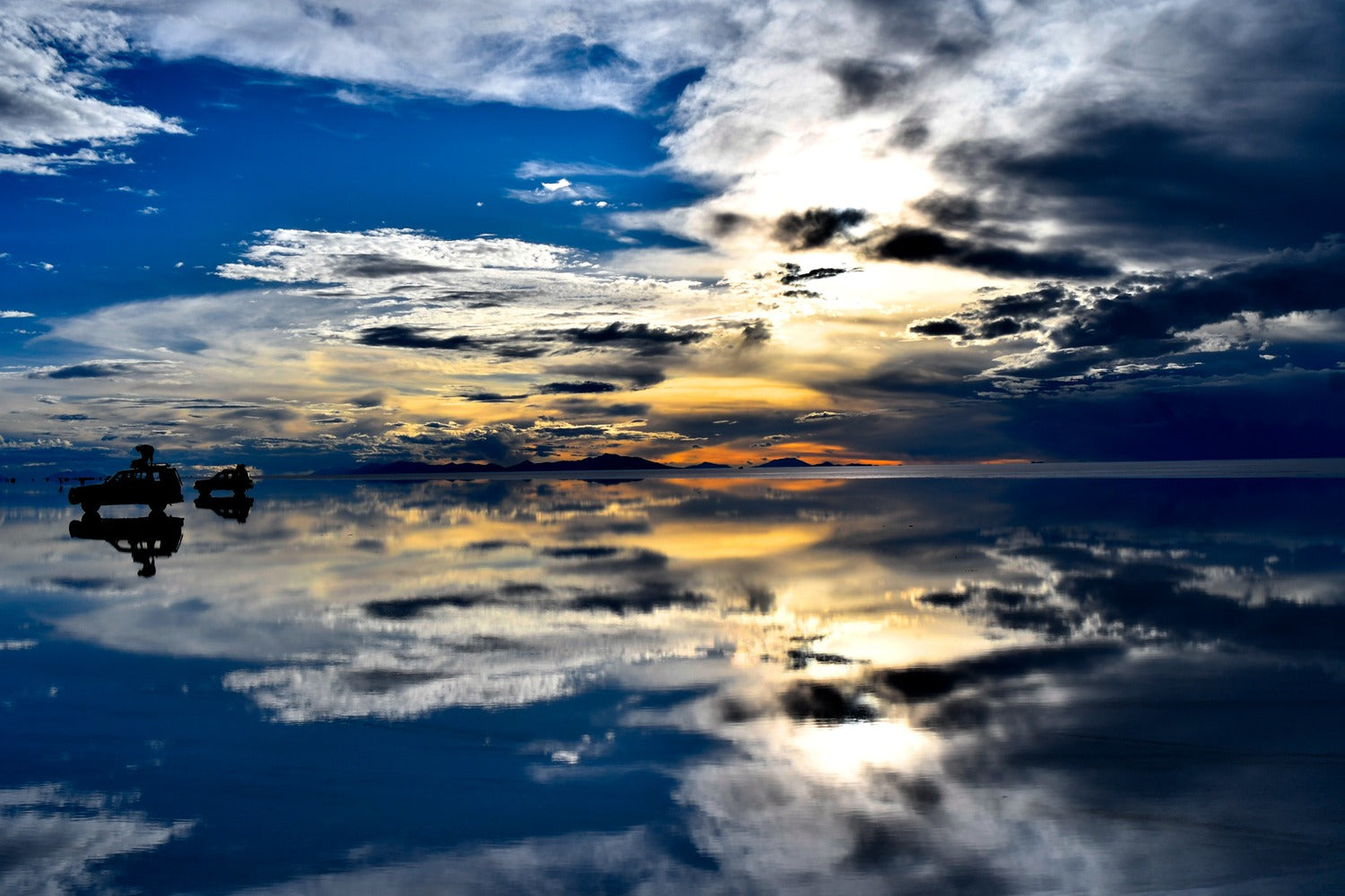 The Uyuni Salt Flats transformed into an immense natural mirror reflect a dramatic sky of clouds and light, creating a surreal scene where the horizon seems to disappear completely.