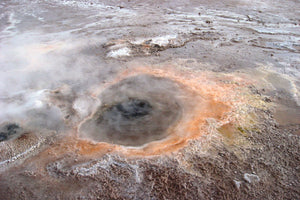 Geothermal area with steam rising from a hot spring, surrounded by a barren landscape.