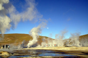 Geothermal activity with steam rising from hot springs against a clear blue sky.
