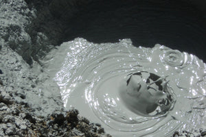 Mud volcano with water bubbling out of it on a rocky surface.