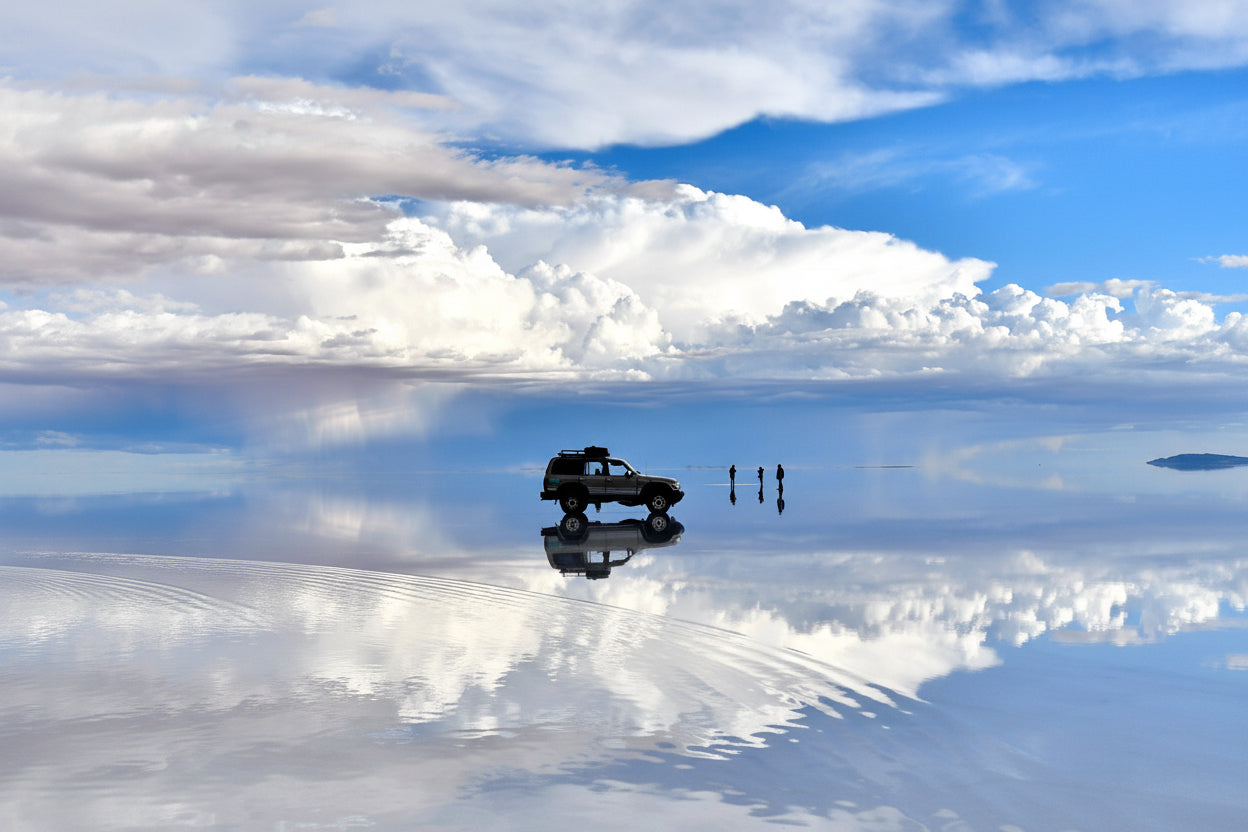 4x4 vehicle and travelers reflected in the mirror effect on the Uyuni Salt Flat, Bolivia