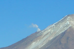 Volcanic eruption with ash cloud on a mountain against a clear blue sky.