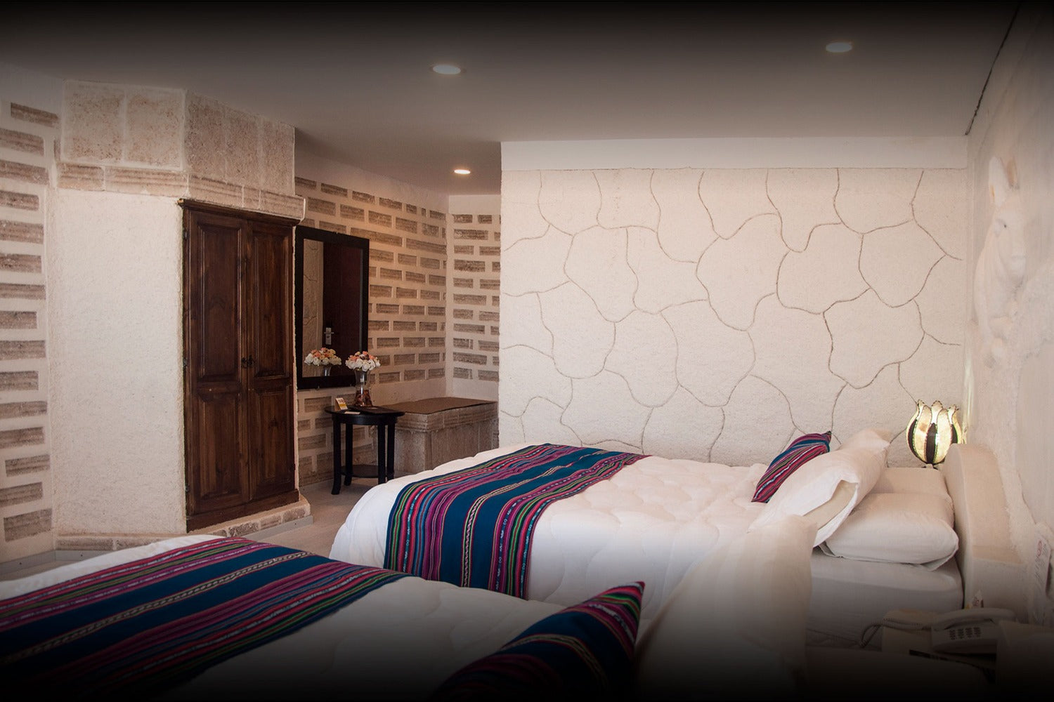 Modern bedroom with stone walls, wooden wardrobe, and bed with striped bedding at Uyuni Salt Flats