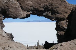 Rocks forming an arch over a Uyuni Salt flats with cacti and mountains in the distance.