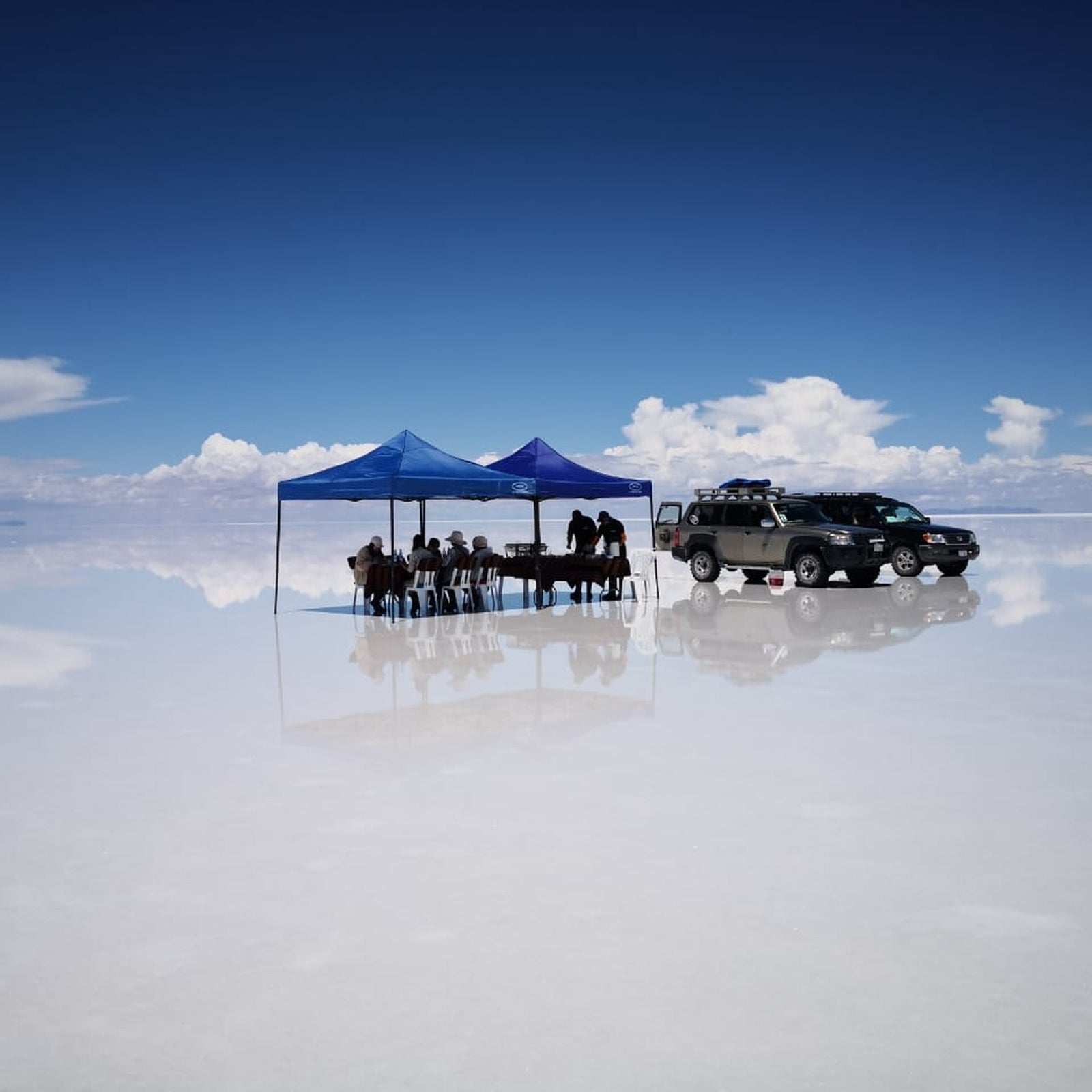 Blue shade tents and 4x4 vehicles on the reflective Uyuni Salt Flat during a private expedition stop.