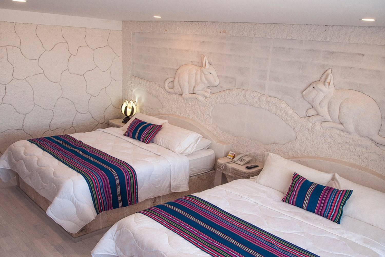 Two beds with colorful bedspreads in a room with stone walls and rabbit sculptures.