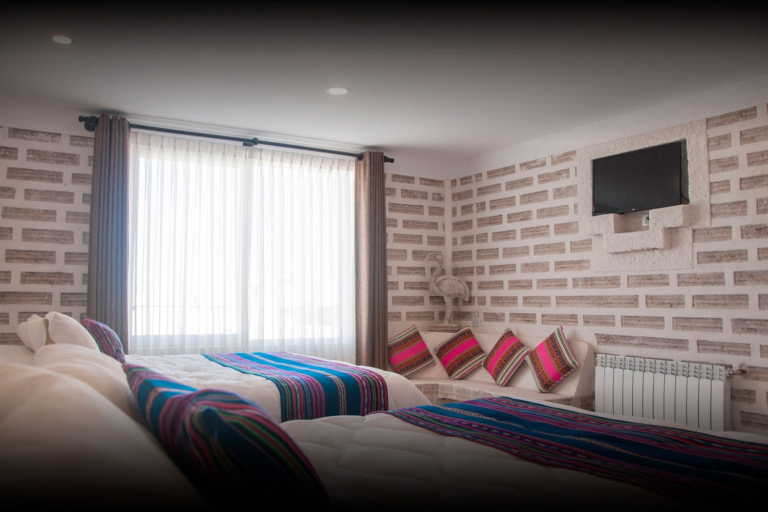 Hotel room with two beds, colorful blankets, and a brick wall.