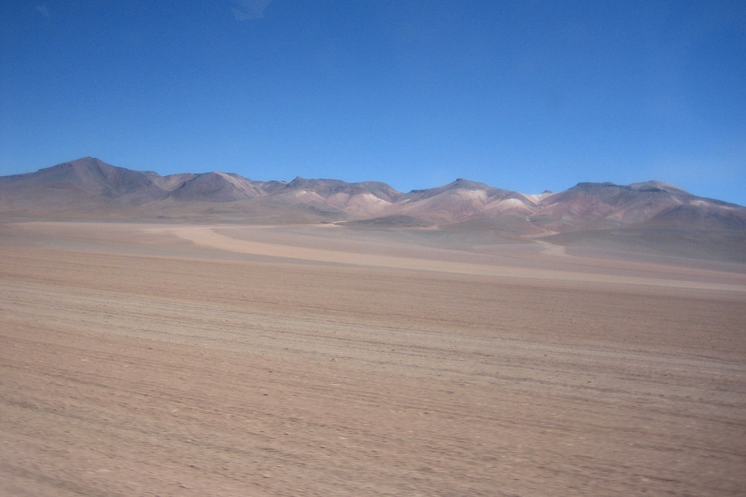 Vast desert plains of the Bolivian Altiplano surrounded by multicolored mountains.