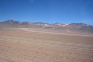 Vast desert plains of the Bolivian Altiplano surrounded by multicolored mountains.