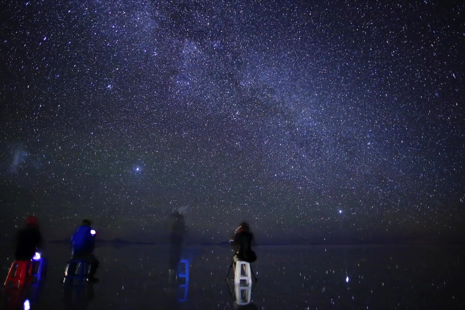 People on stools under a starry night sky at Uyuni salt flat
