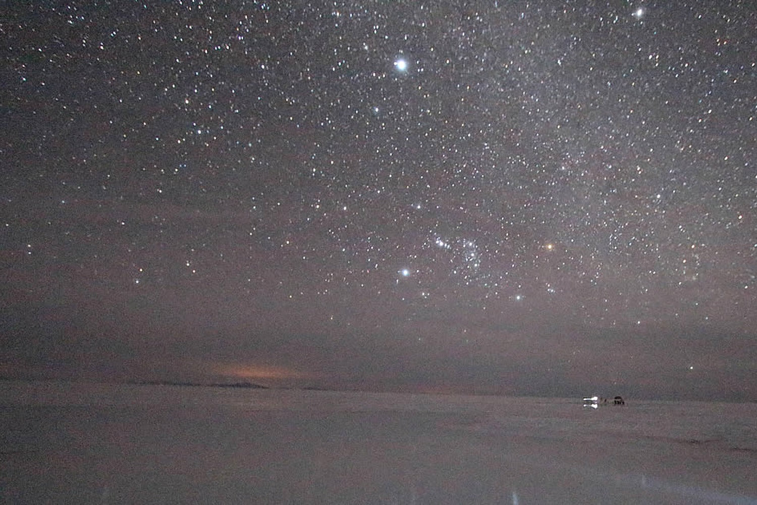Starry night sky over Uyuni salt flat landscape with a car in the distance.