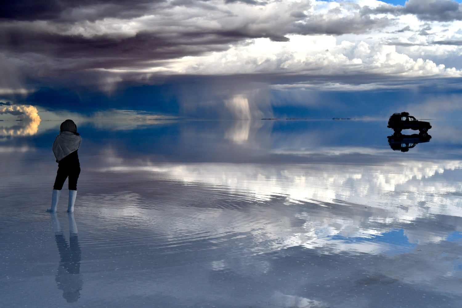 Person standing on a reflective Uyuni salt flat surface with clouds mirrored above