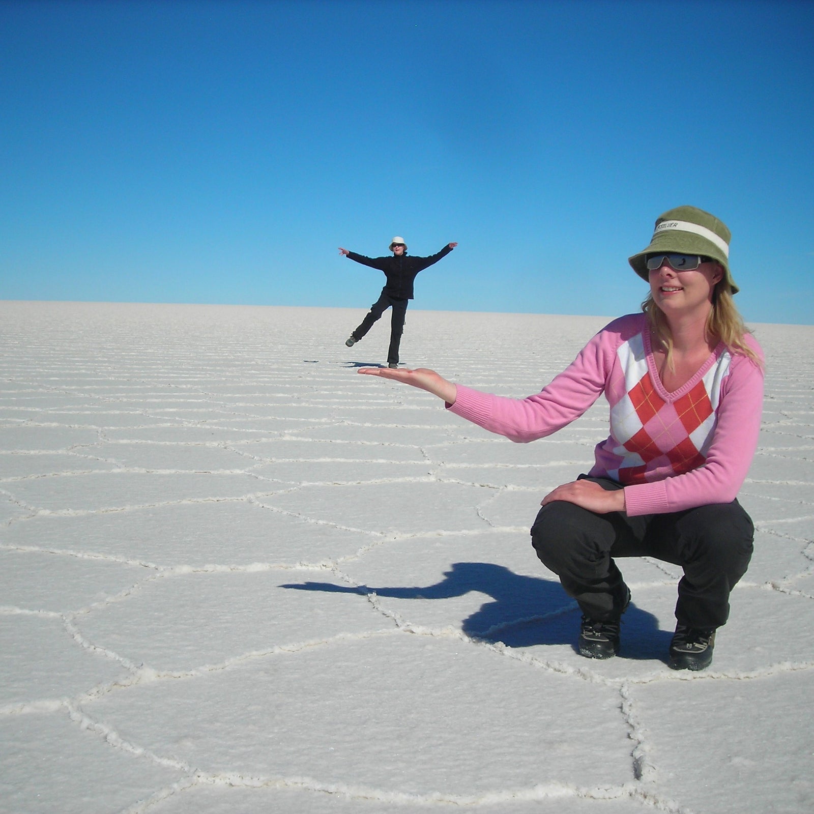 Trine Madsen Møller posing on the Uyuni Salt Flat in a playful perspective shot under a clear blue sky.