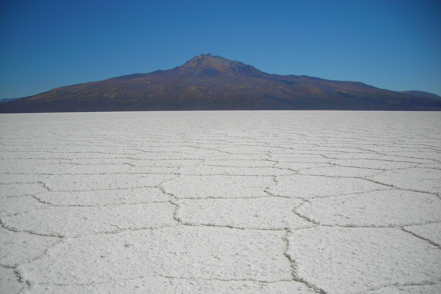 Classic panorama of the Uyuni Salt Flats with its iconic hexagonal salt formations stretching toward a majestic Andean mountain.