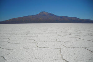 Classic panorama of the Uyuni Salt Flats with its iconic hexagonal salt formations stretching toward a majestic Andean mountain.