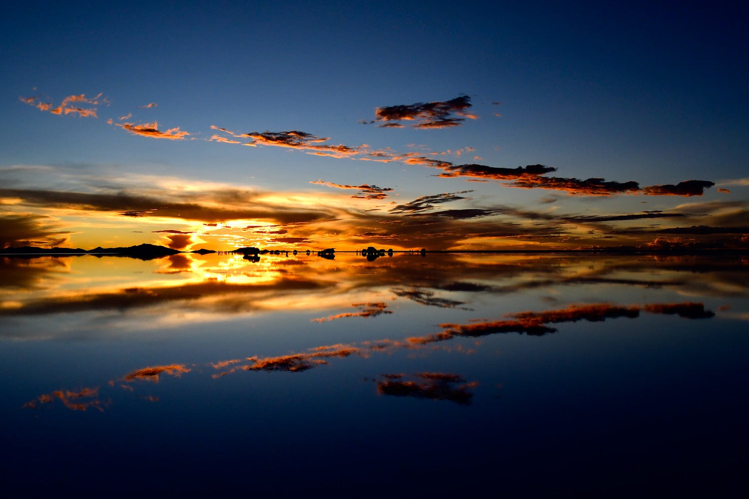 Sunset reflections across the Uyuni Salt Flat with dark clouds mirrored in shallow water.