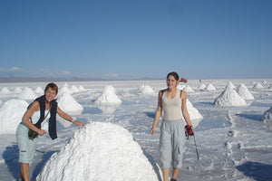 Two people exploring a salt flat landscape with large salt formations.