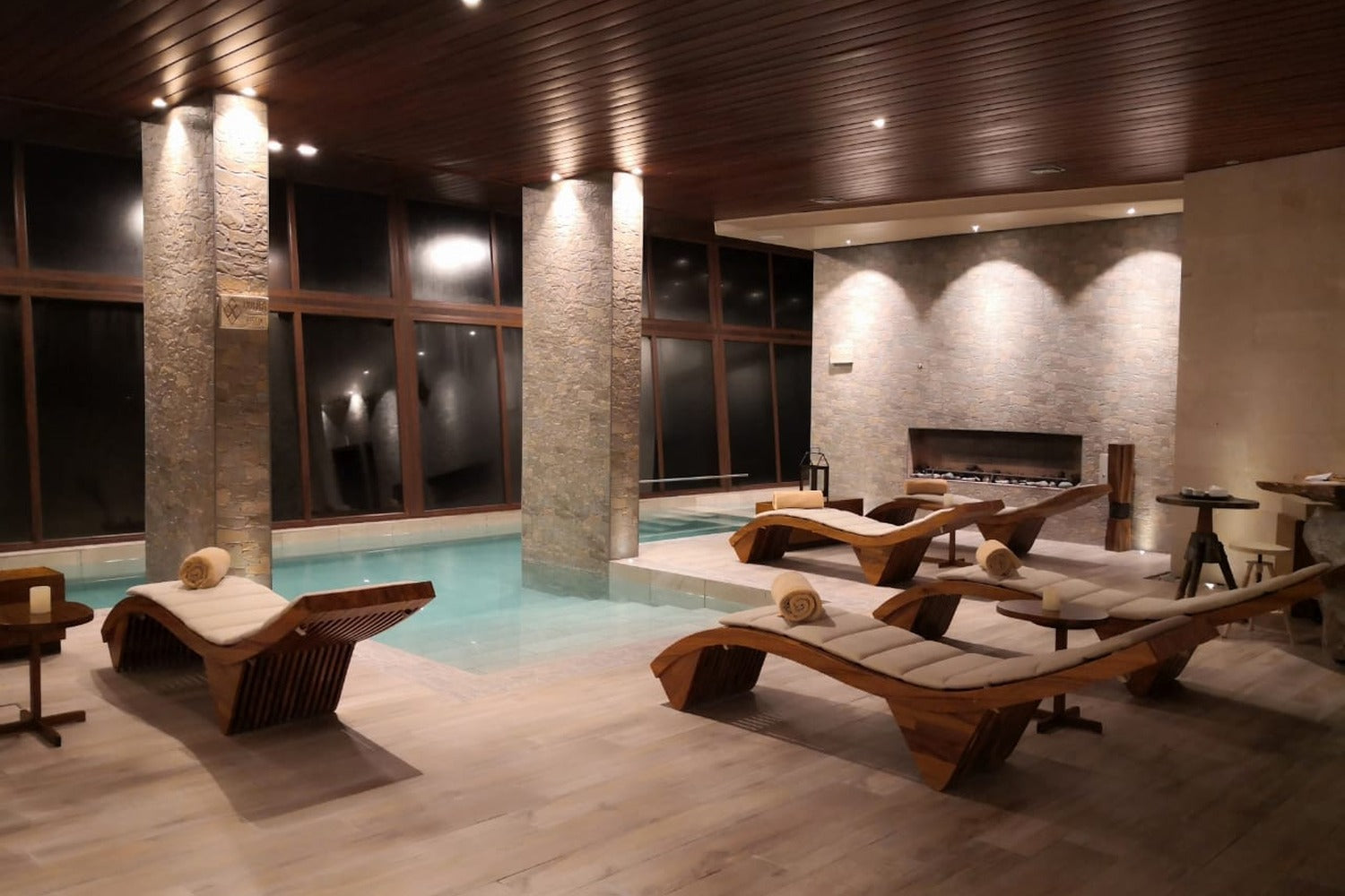 Indoor pool area with lounge chairs and a fireplace.