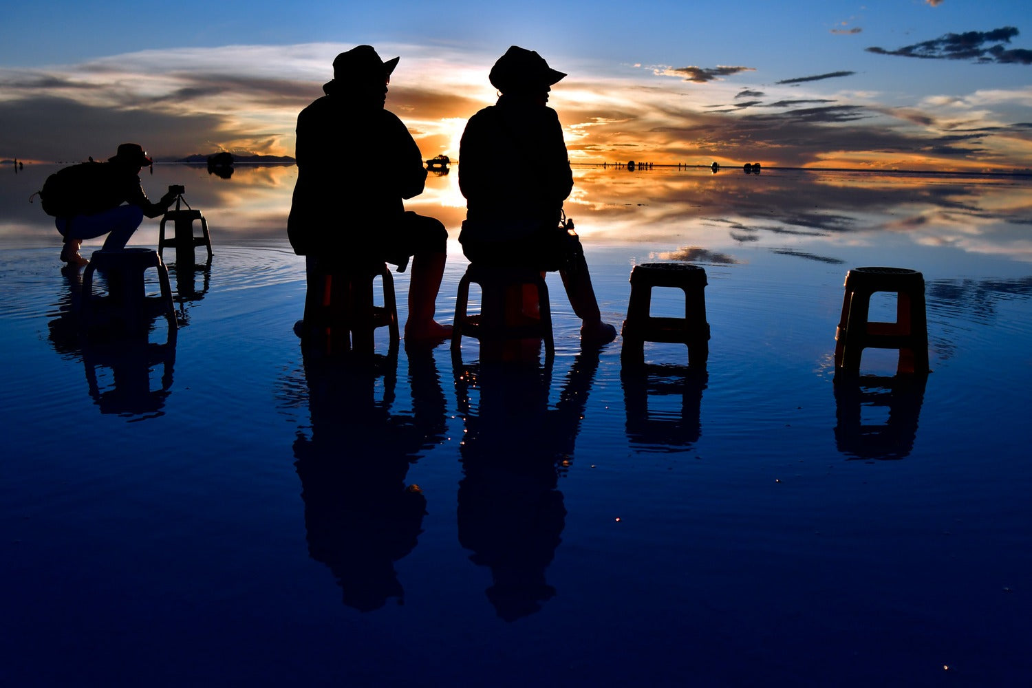 Travelers enjoying a magical sunset over the Uyuni Salt Flats, contemplating the spectacle of colors and endless reflections that make every moment unforgettable.