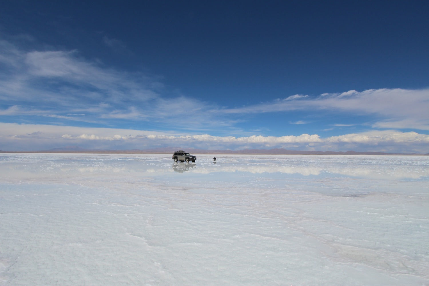 4WD vehicle crossing the vast Uyuni Salt Flats during mirror season.