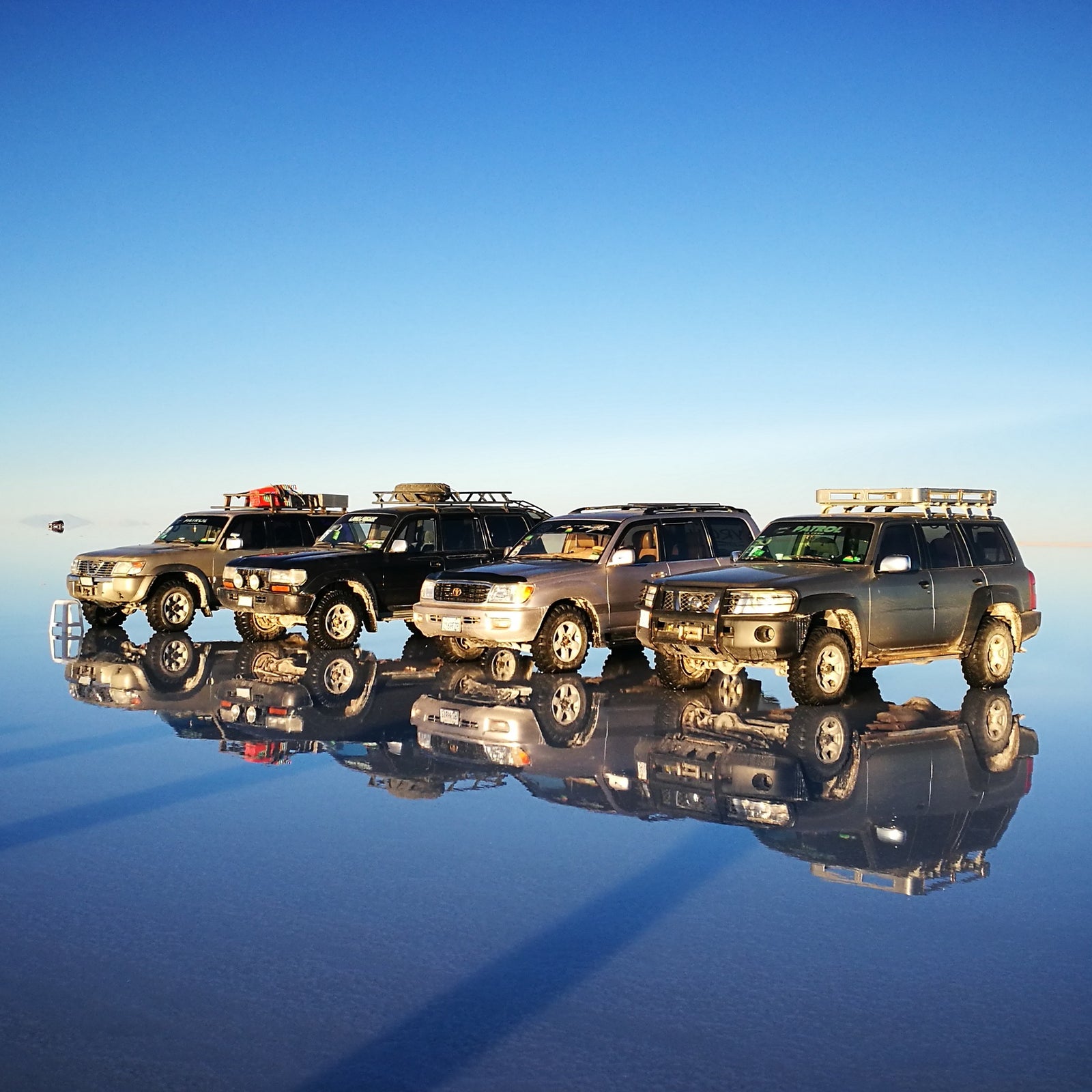 4x4 vehicles ready to explore the Uyuni Salt Flats during mirror season, perfectly reflected on the flooded surface.