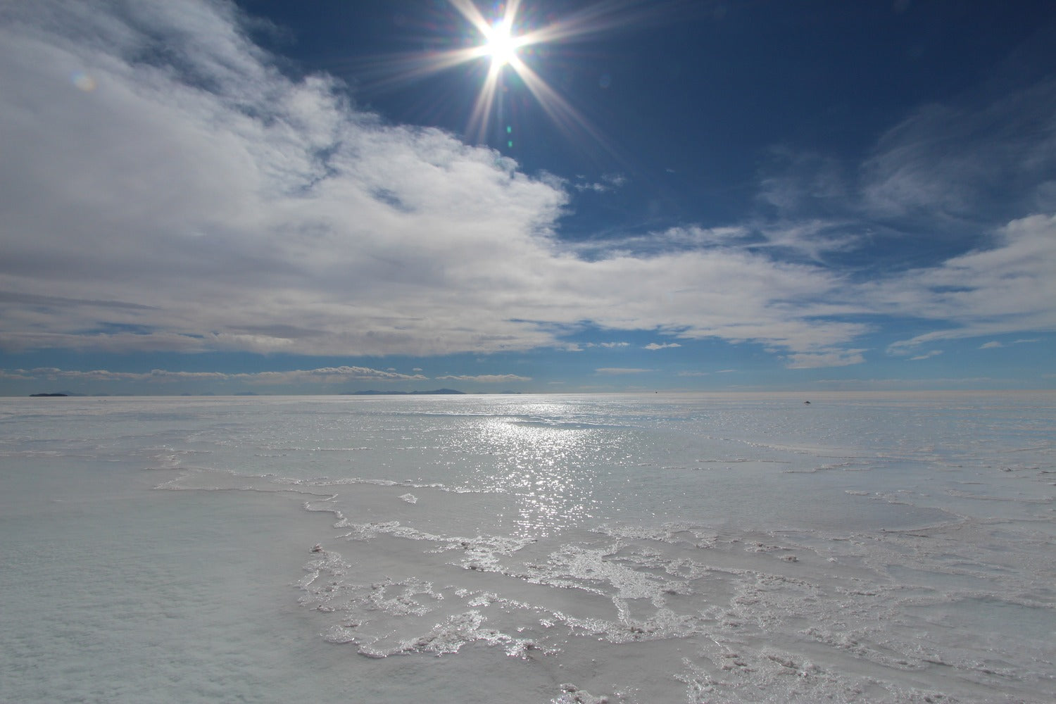 Uyuni salt flat surface with a clear blue sky and sun shining through clouds