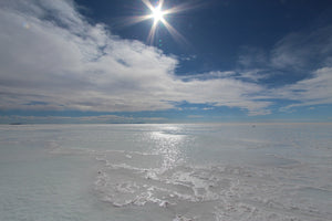 Uyuni salt flat surface with a clear blue sky and sun shining through clouds