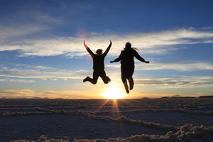 Two people jumping in the air with a sunset in the background at Uyuni salt flat, Bolivai