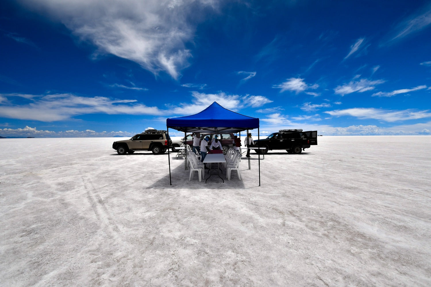 Blue tent at Uyuni salt flat with vehicles in the background under a blue sky.