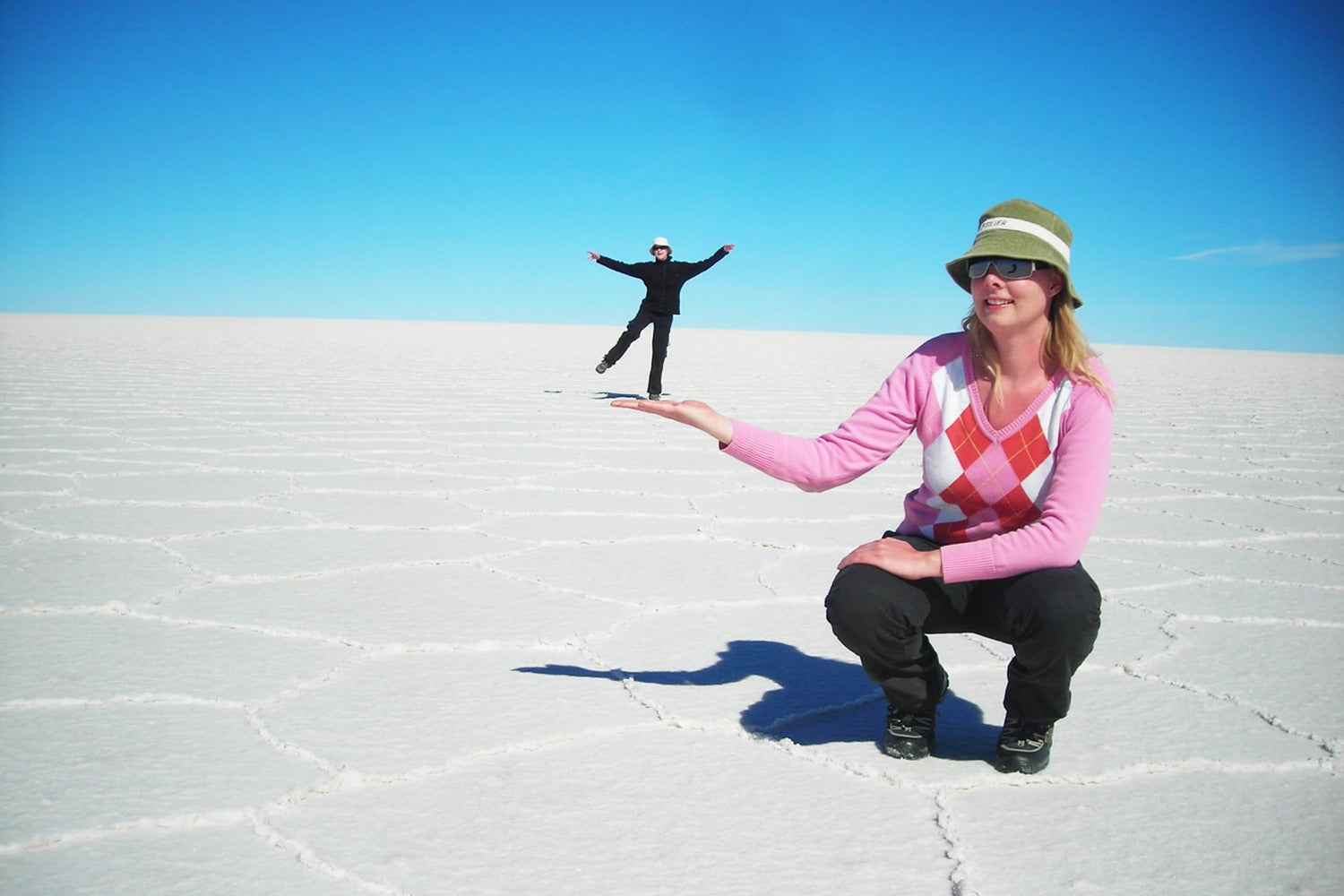 Person posing with a smaller person in the distance at Uyuni salt flat under a clear blue sky.