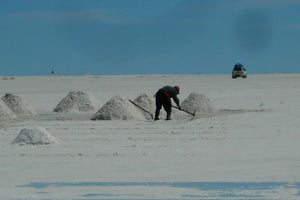 Person working with a tool on Uyuni salt flats with a vehicle in the distance.