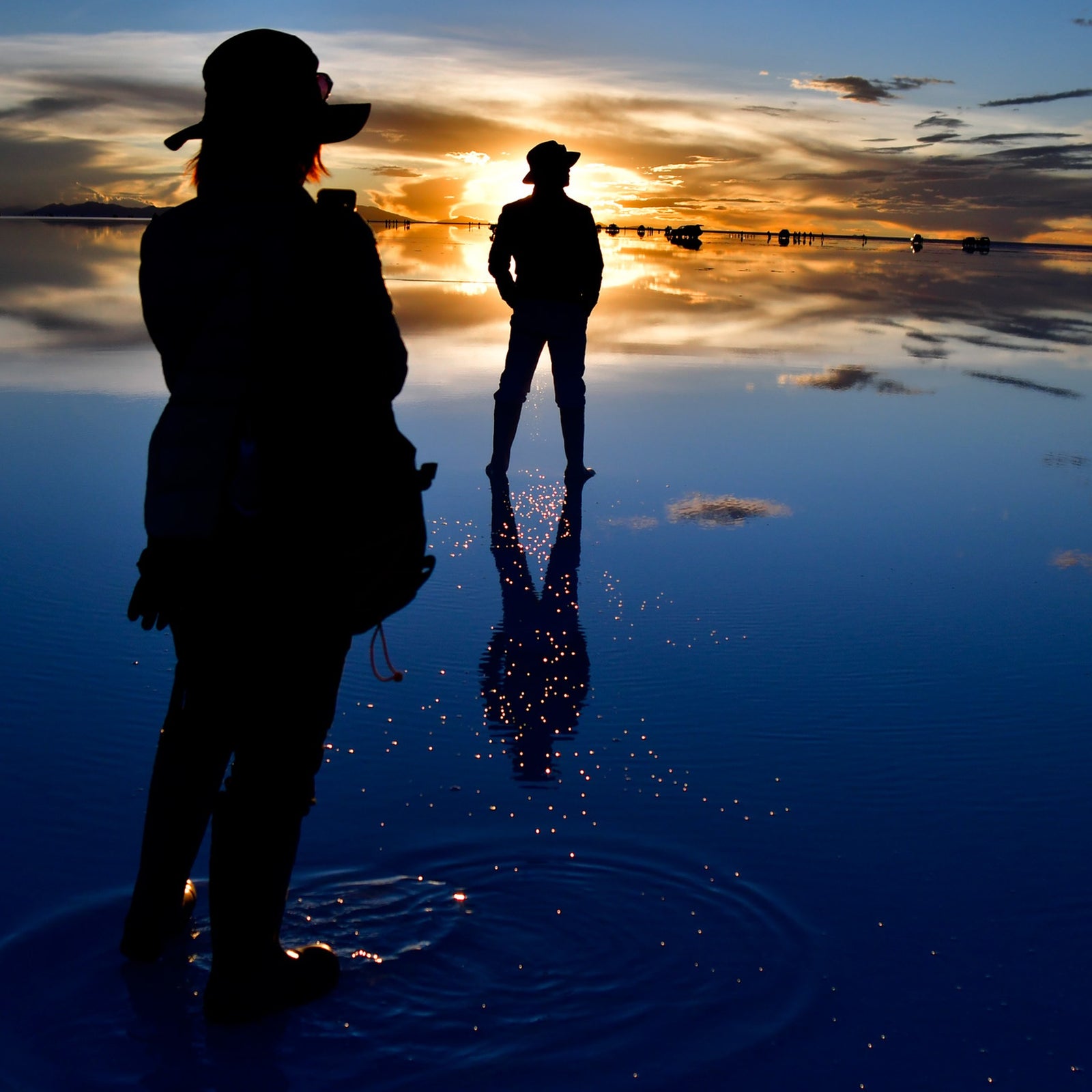 Travelers watching the sunset over the  Uyuni salt flats and the reflection on the water