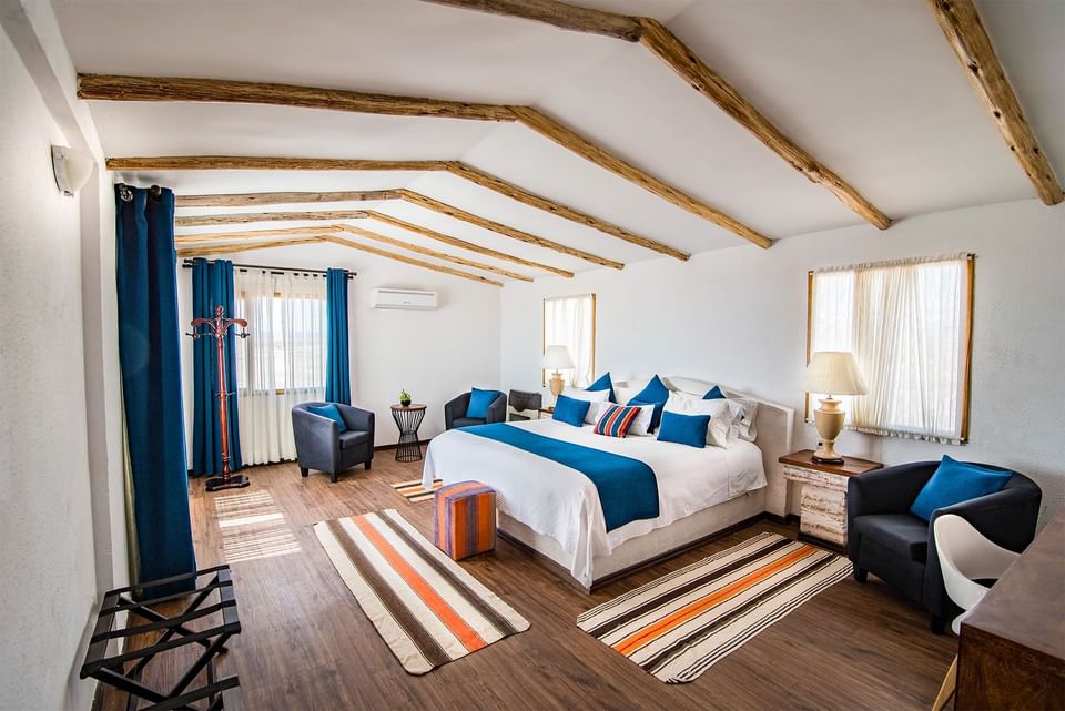 Modern bedroom with wooden beams, bed, chairs, and decor.