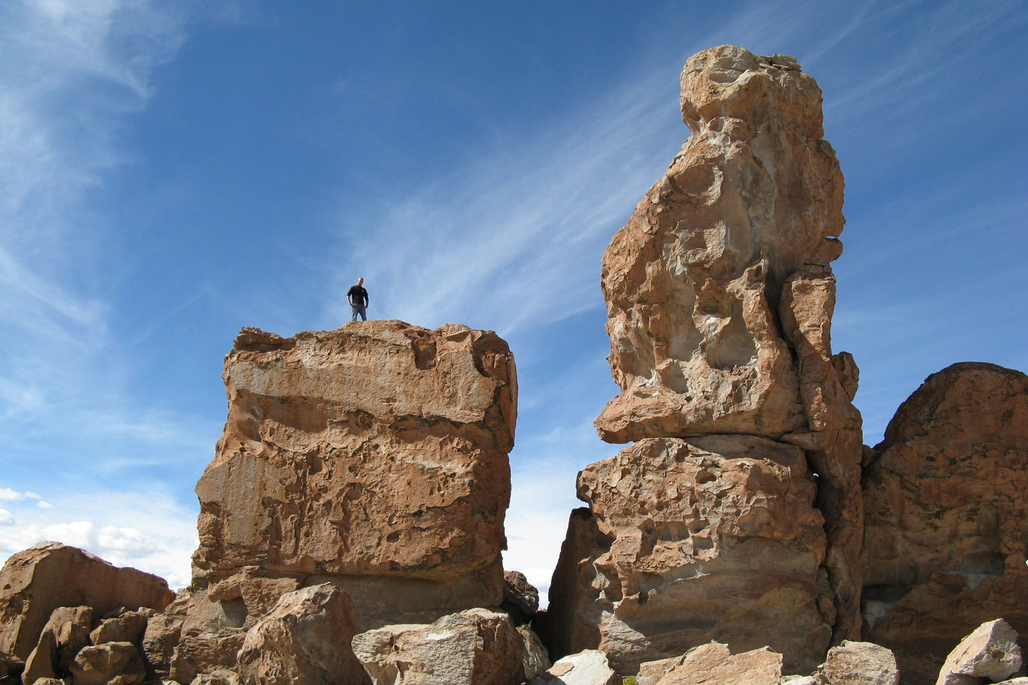 traveller standing on a large rock formation against a blue sky in valle de las rocas Lipez, Bolivia